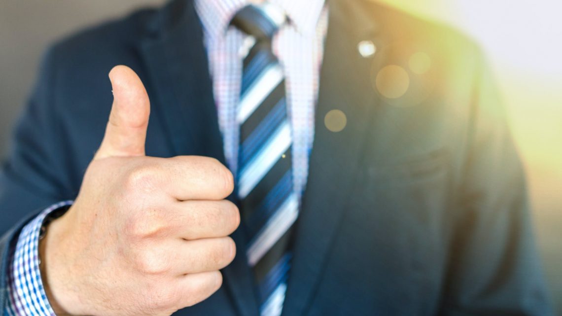 close up photo of man wearing black suit jacket doing thumbs up gesture
